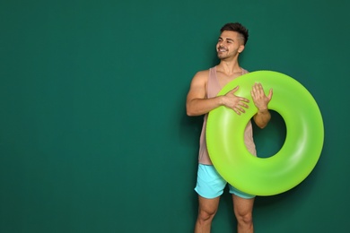 Photo of Funny young man with bright inflatable ring on dark green background, space for text