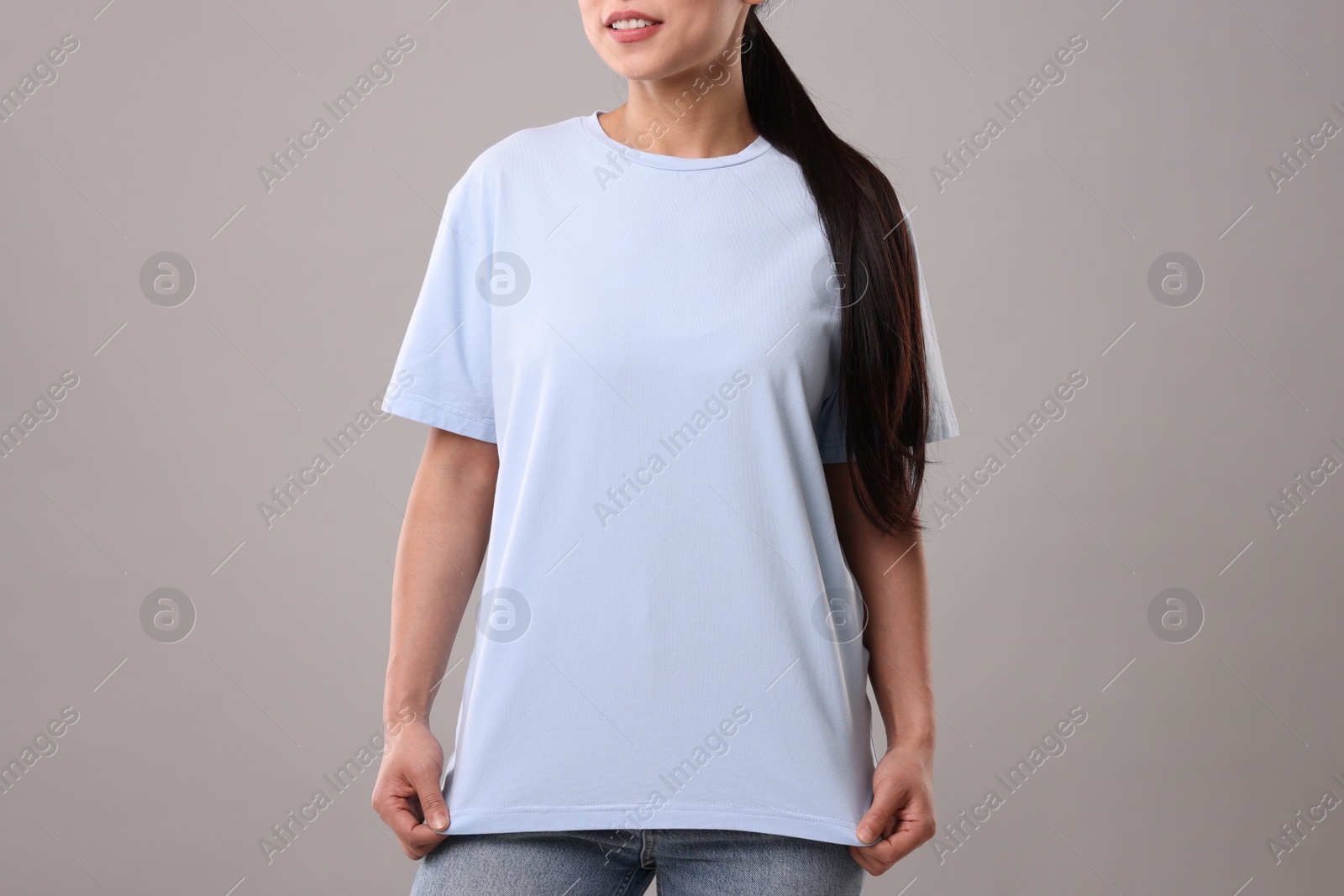 Photo of Woman wearing light blue t-shirt on grey background, closeup