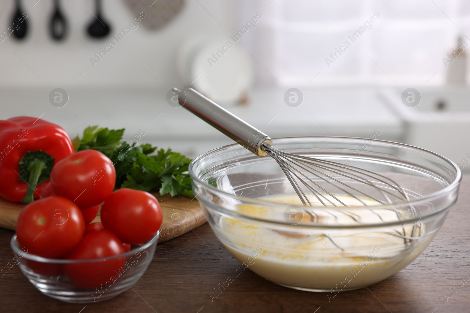 Photo of Whisk, bowl, beaten eggs and other ingredients on wooden table indoors