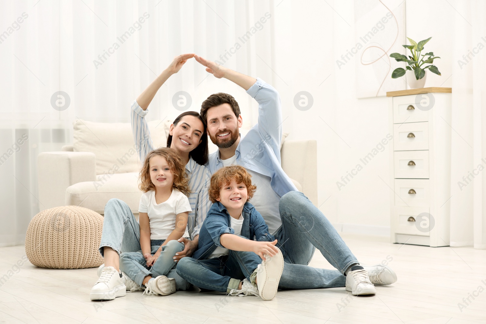 Photo of Family housing concept. Happy woman and her husband forming roof with their hands while sitting with kids on floor at home