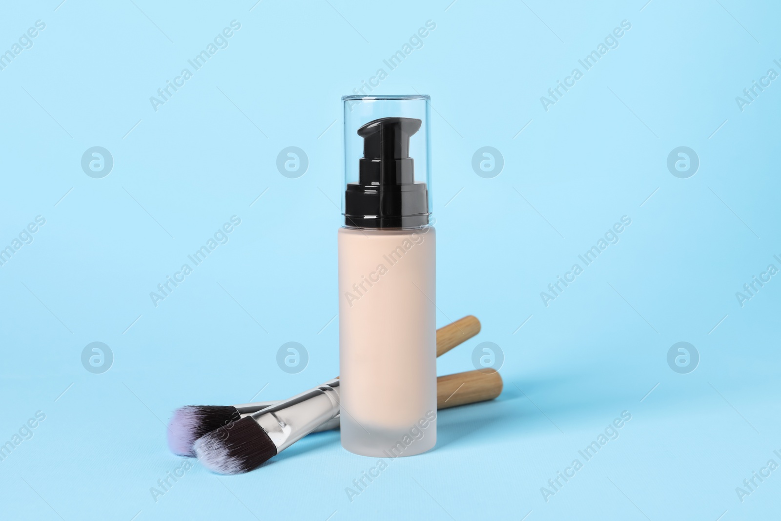 Photo of Bottle of skin foundation and brushes on light blue background. Makeup product