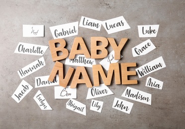 Photo of Paper sheets with different baby names and wooden letters on grey background, flat lay