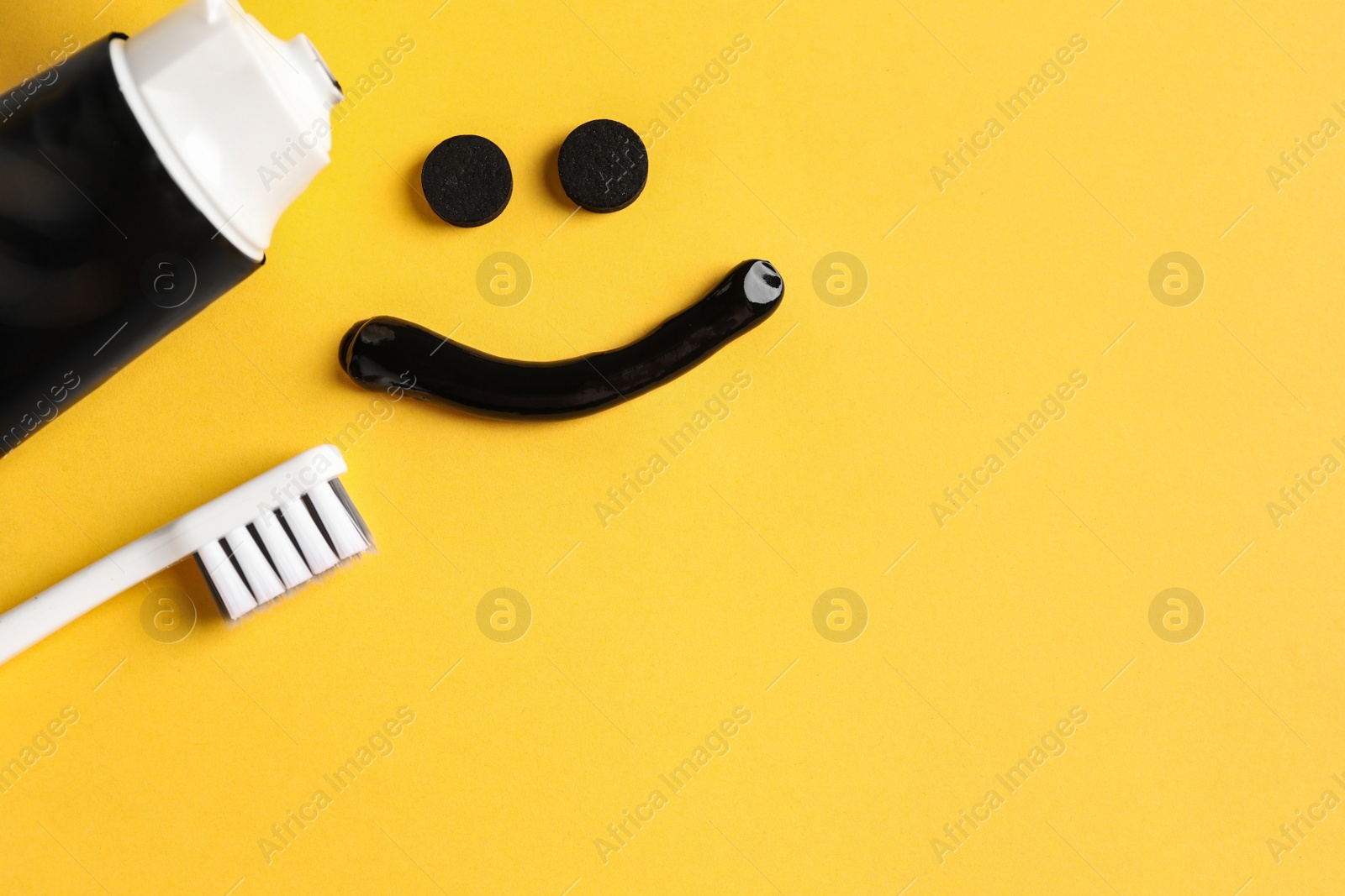 Photo of Flat lay composition with charcoal toothpaste on yellow background. Space for text