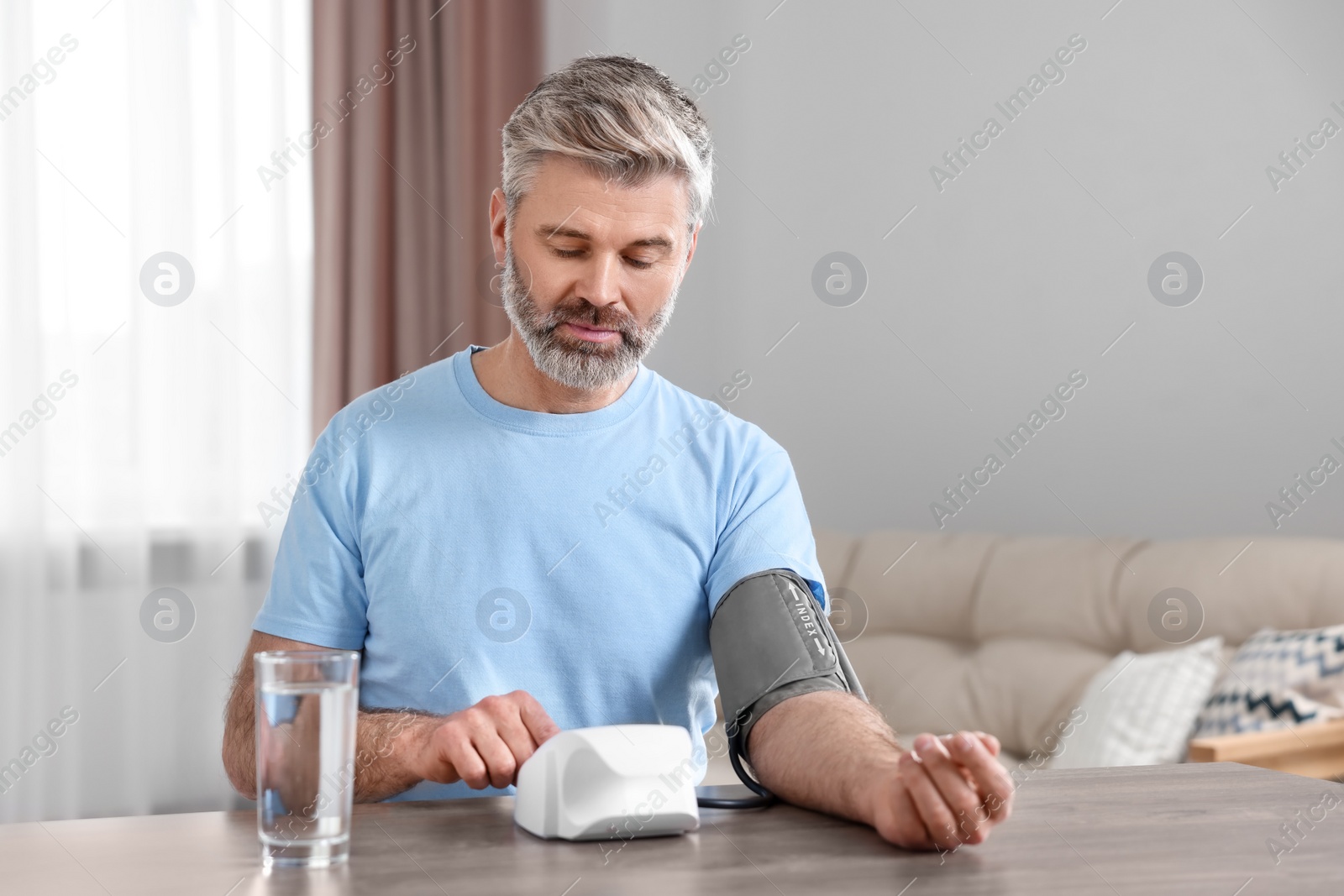 Photo of Man measuring blood pressure at table indoors