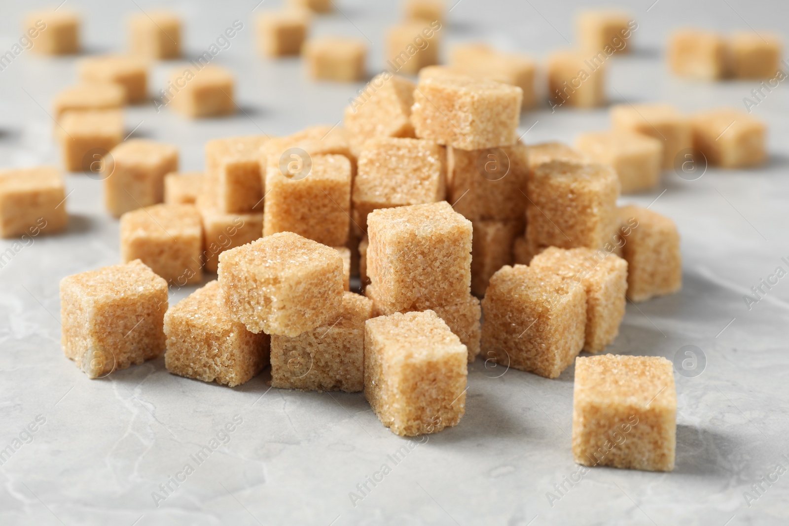 Photo of Heap of brown sugar cubes on light grey marble table, closeup