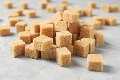 Photo of Heapbrown sugar cubes on light grey marble table, closeup