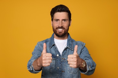 Handsome bearded man showing thumbs up on orange background