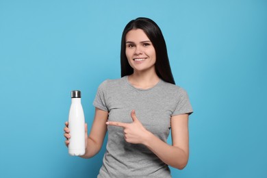 Young woman with thermo bottle on light blue background