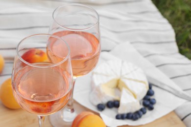 Glasses of delicious rose wine and food on picnic blanket outdoors, closeup