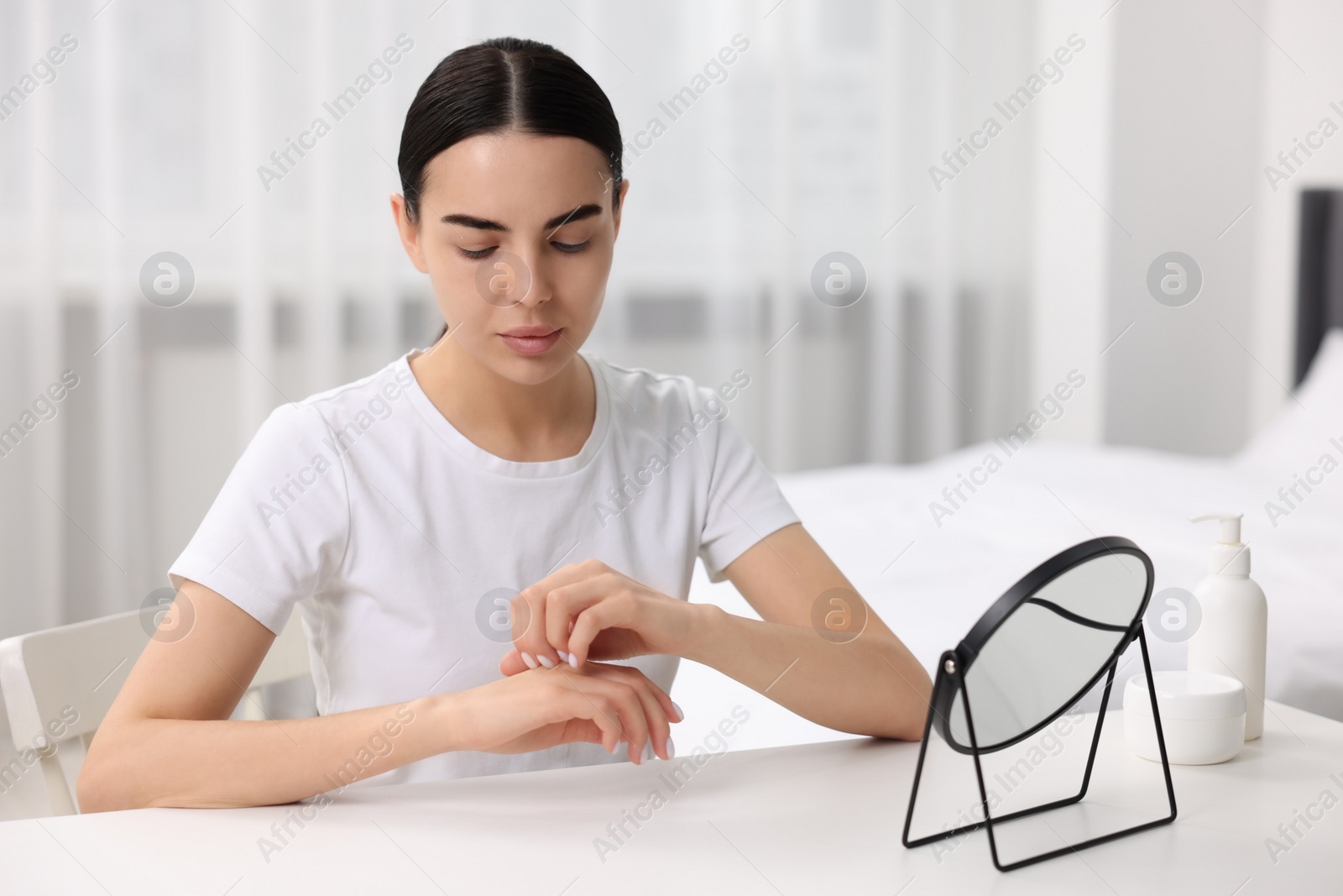 Photo of Woman with dry skin checking her arm at table indoors