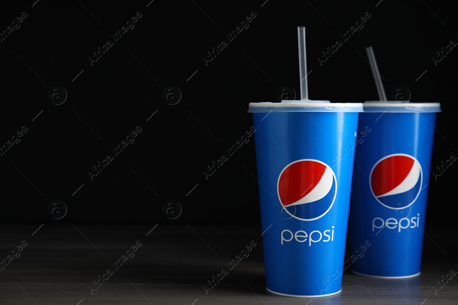 Photo of MYKOLAIV, UKRAINE - JUNE 9, 2021: Paper Pepsi cups on wooden table against dark background, space for text