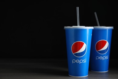 MYKOLAIV, UKRAINE - JUNE 9, 2021: Paper Pepsi cups on wooden table against dark background, space for text