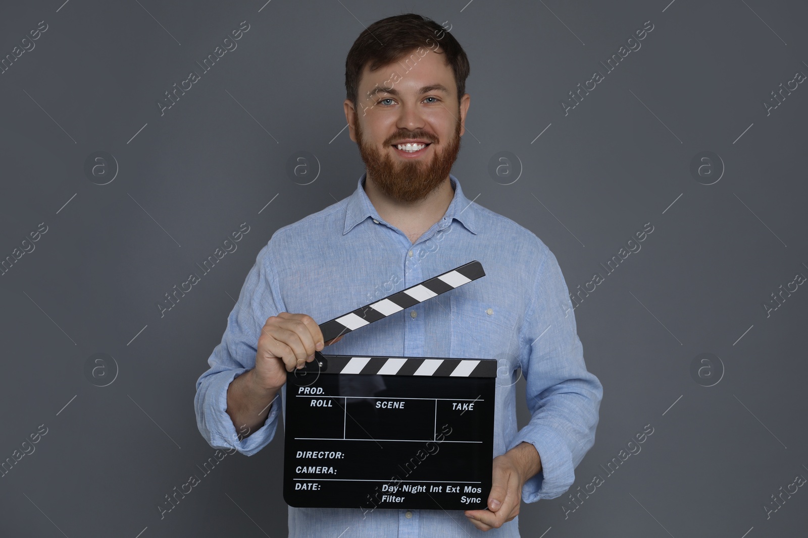 Photo of Making movie. Smiling man with clapperboard on grey background