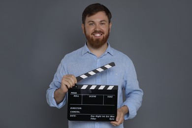 Making movie. Smiling man with clapperboard on grey background