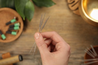 Woman holding many acupuncture needles over wooden table, closeup