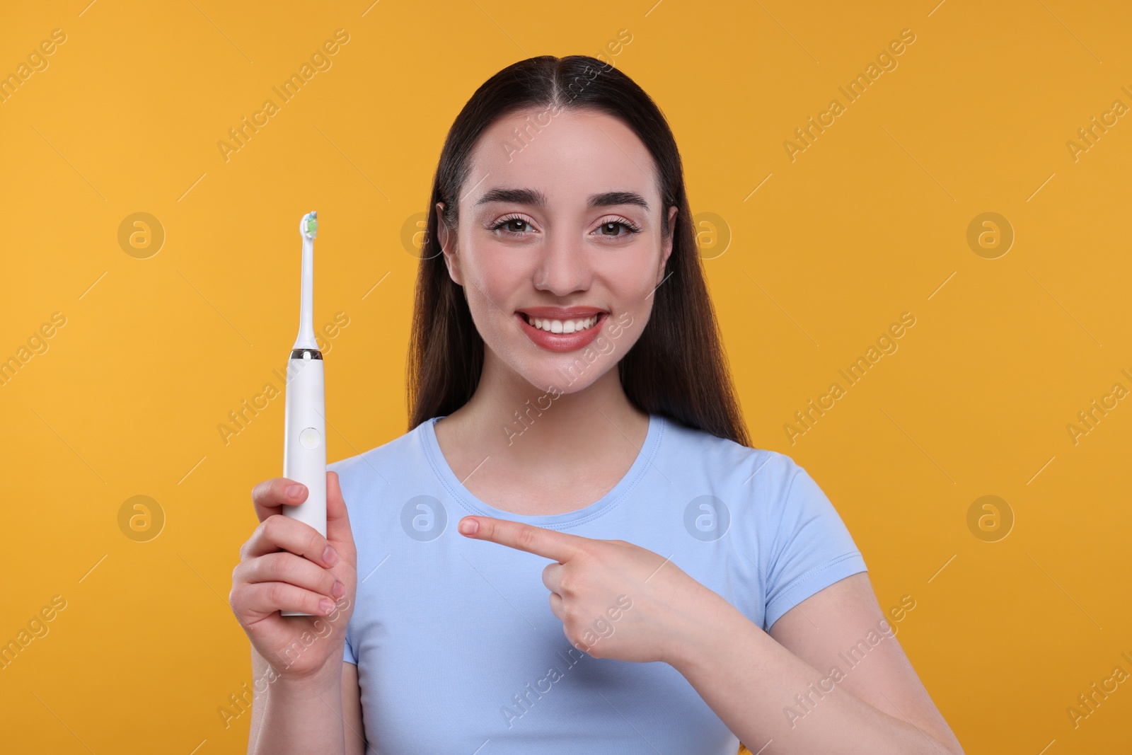 Photo of Happy young woman holding electric toothbrush on yellow background