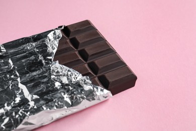 Photo of Delicious dark chocolate bar wrapped in foil on pink background. Space for text