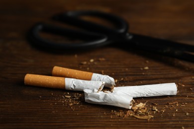 Photo of Cut cigarettes and scissors on wooden table, closeup. Quitting smoking concept