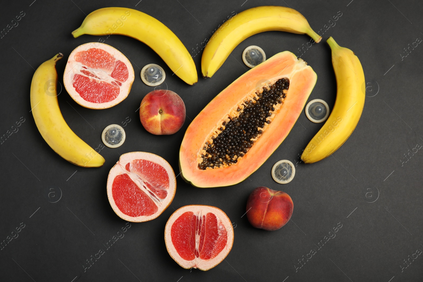 Photo of Flat lay composition with condoms and exotic fruits on black background. Erotic concept