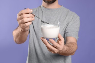 Photo of Man with delicious yogurt and spoon on violet background, closeup