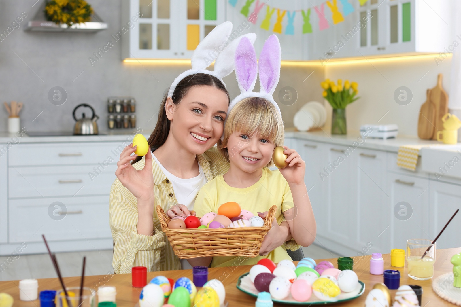 Photo of Mother and her cute son with Easter eggs at table in kitchen