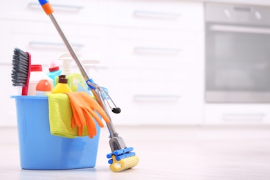 Photo of Bucket with cleaning supplies on floor in kitchen. Space for text