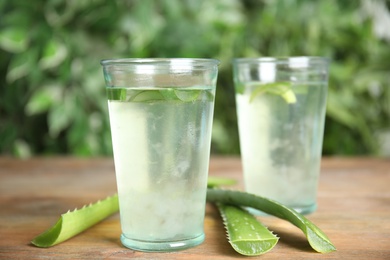 Photo of Fresh aloe drink in glasses and leaves on wooden table