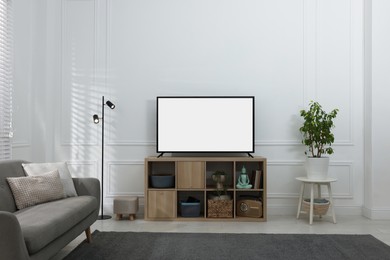 Image of Modern TV on cabinet, floor lamp and beautiful houseplant near light wall indoors. Interior design