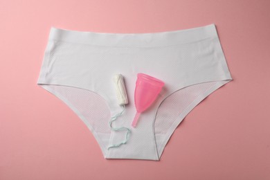 Photo of Menstrual cup, tampon and panties on pink background, flat lay