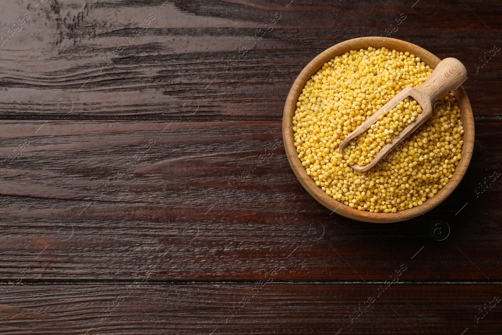 Photo of Millet groats in bowl and scoop on wooden table, top view. Space for text