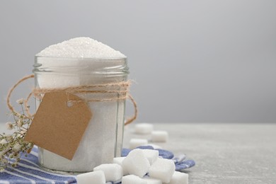 Glass jar of granulated sugar and cubes on table, space for text