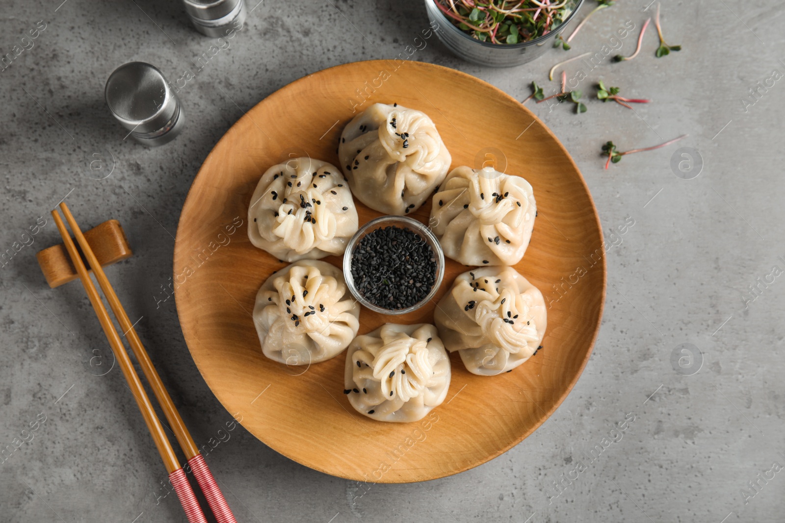 Photo of Wooden plate with tasty baozi dumplings and sesame seeds served on grey table, top view