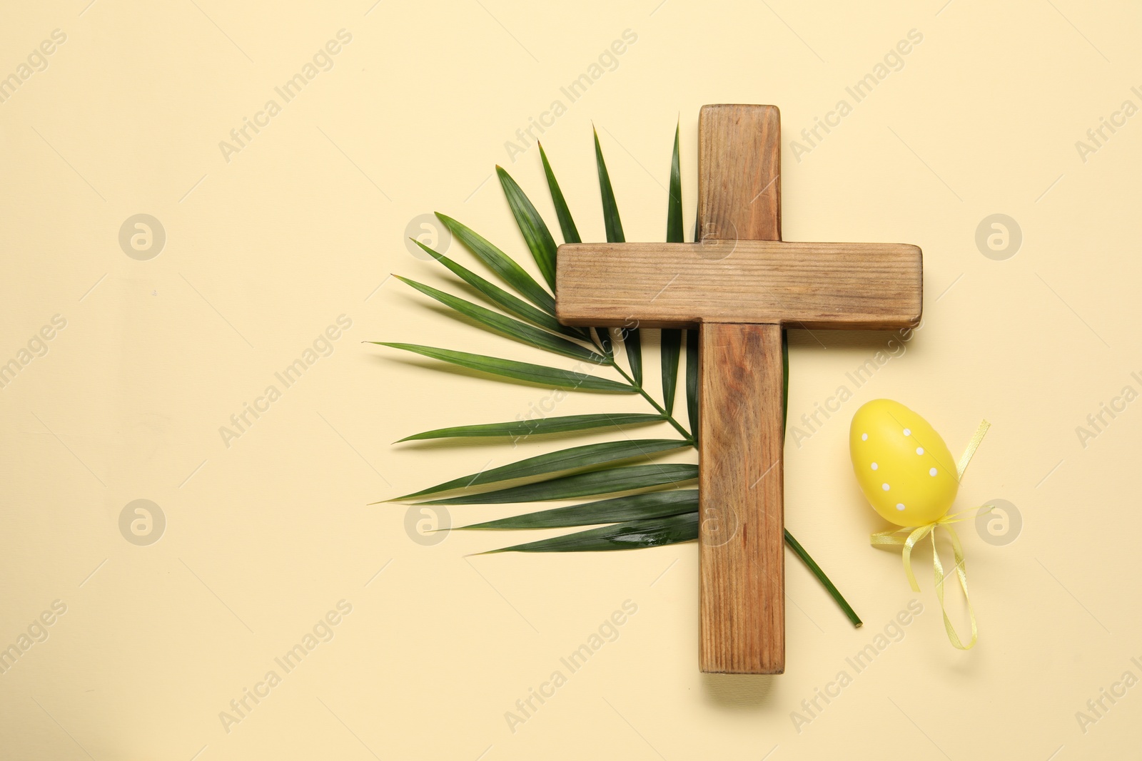 Photo of Wooden cross, painted Easter egg and palm leaf on beige background, top view. Space for text