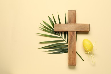 Wooden cross, painted Easter egg and palm leaf on beige background, top view. Space for text