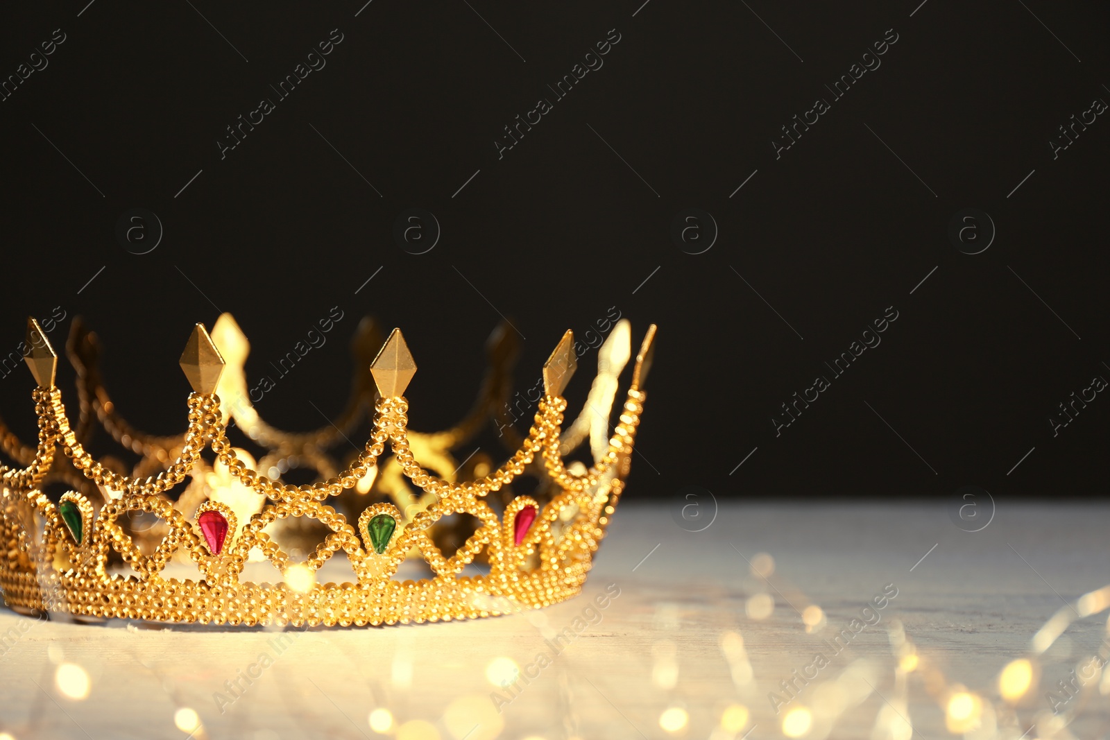 Photo of Beautiful golden crown and fairy lights on black background, space for text. Fantasy item