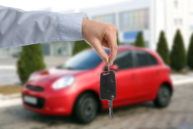 Image of Car buying. Man holding key against blurred automobile, closeup