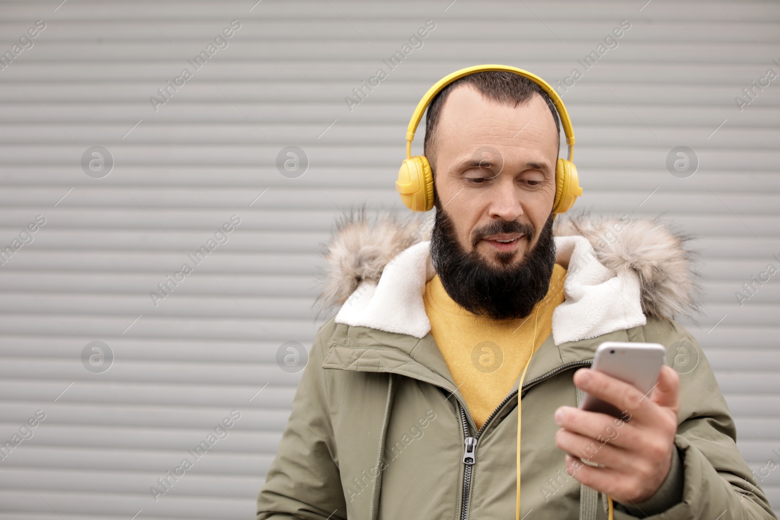 Photo of Mature man with headphones listening to music near light wall. Space for text