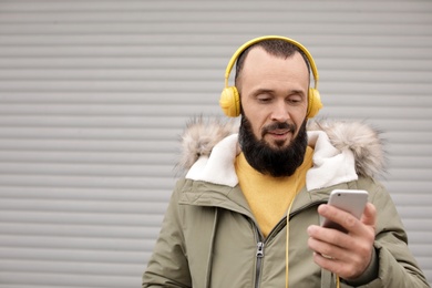 Mature man with headphones listening to music near light wall. Space for text