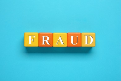 Photo of Word Fraud of wooden cubes with letters on light blue background, flat lay