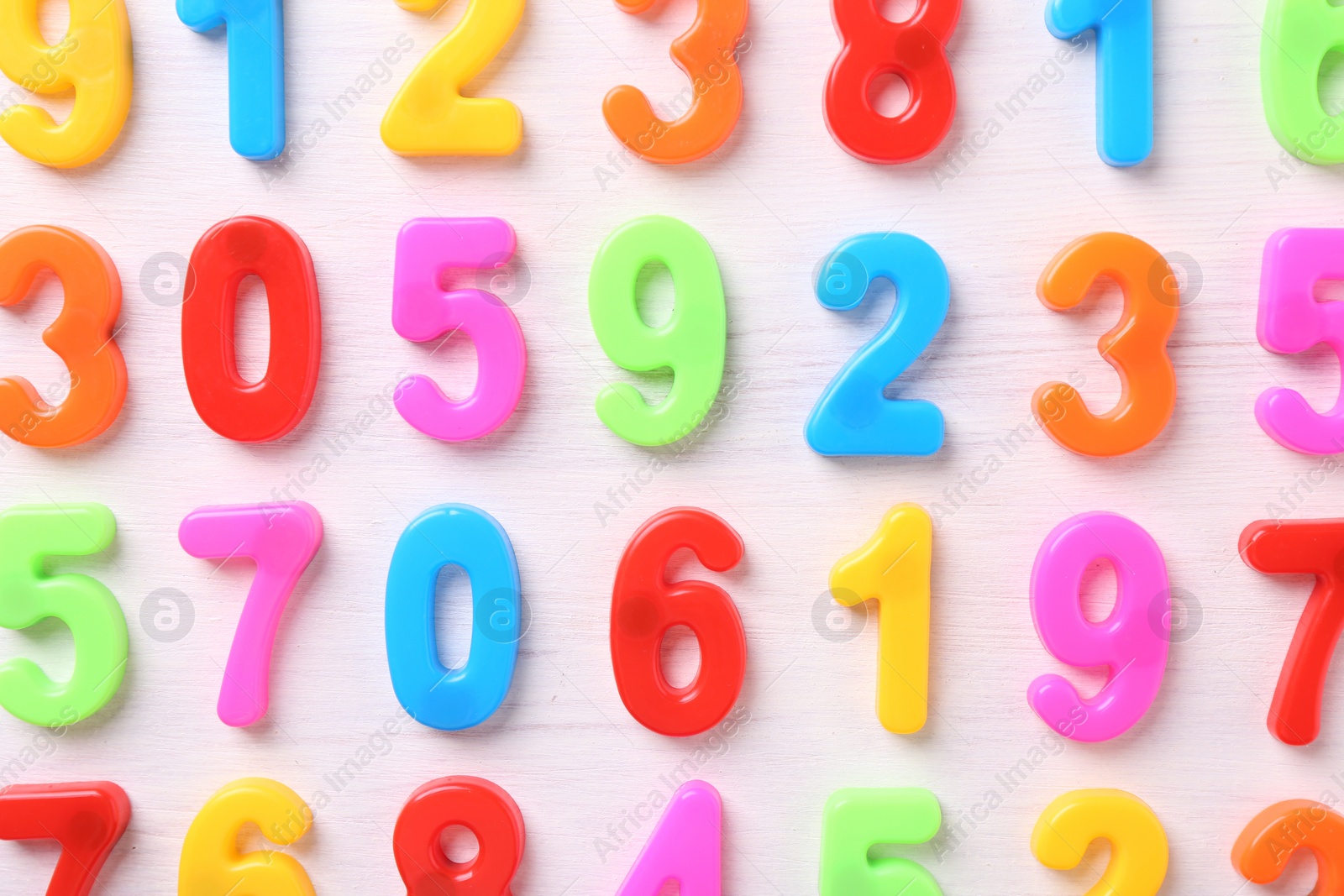 Photo of Colorful numbers on white wooden school desk, flat lay