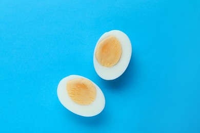 Halves of fresh hard boiled egg on light blue background, flat lay