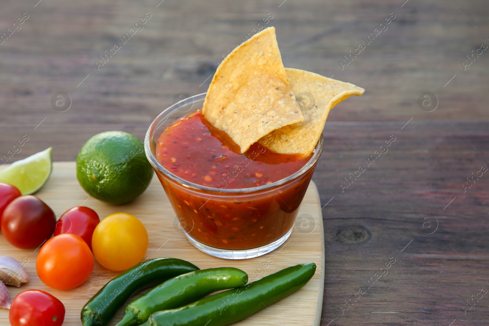 Photo of Tasty salsa sauce with tortilla chips and ingredients on wooden table, closeup