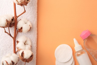 Flat lay composition with makeup remover and cotton flowers on pale orange background, space for text