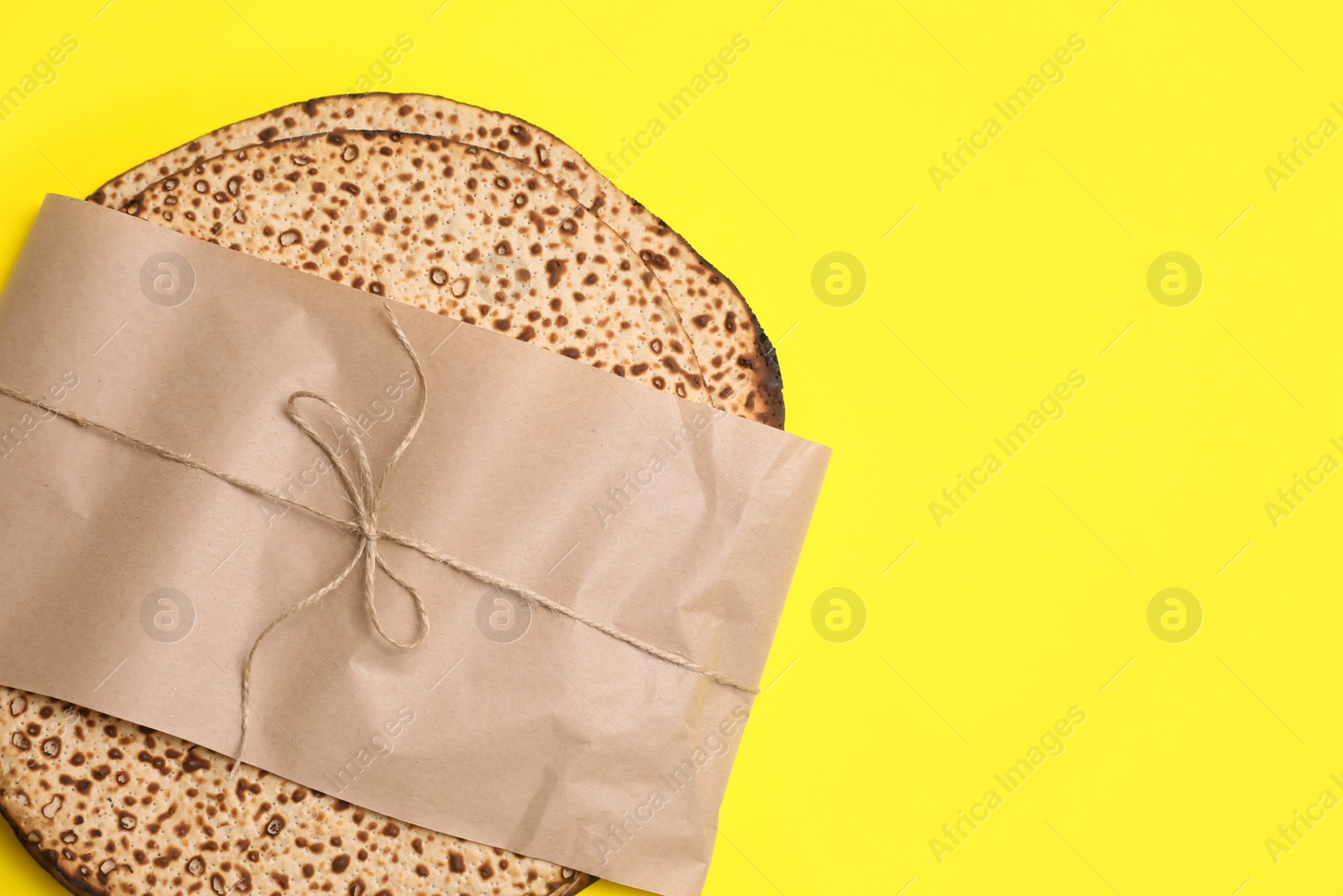 Photo of Top view of tasty matzos wrapped with paper on yellow background, space for text. Passover (Pesach) celebration