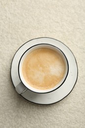 Photo of Tasty cappuccino in cup and saucer on light textured table, top view