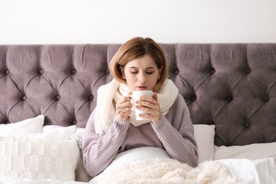 Photo of Sick woman with cup of hot drink suffering from cold in bed