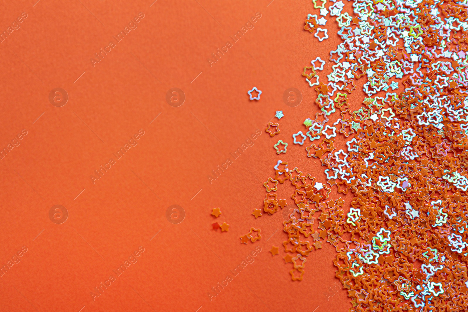 Photo of Shiny bright star shaped glitter on orange background. Space for text