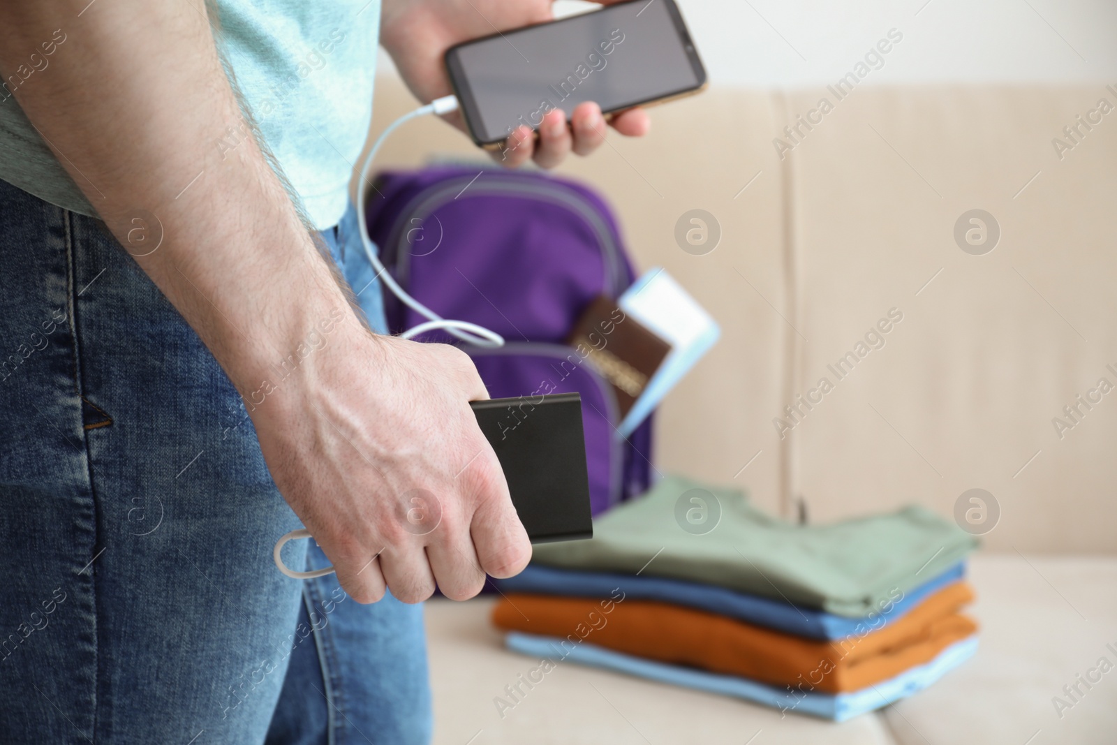 Photo of Man charging mobile phone with power bank while getting ready for travel, closeup