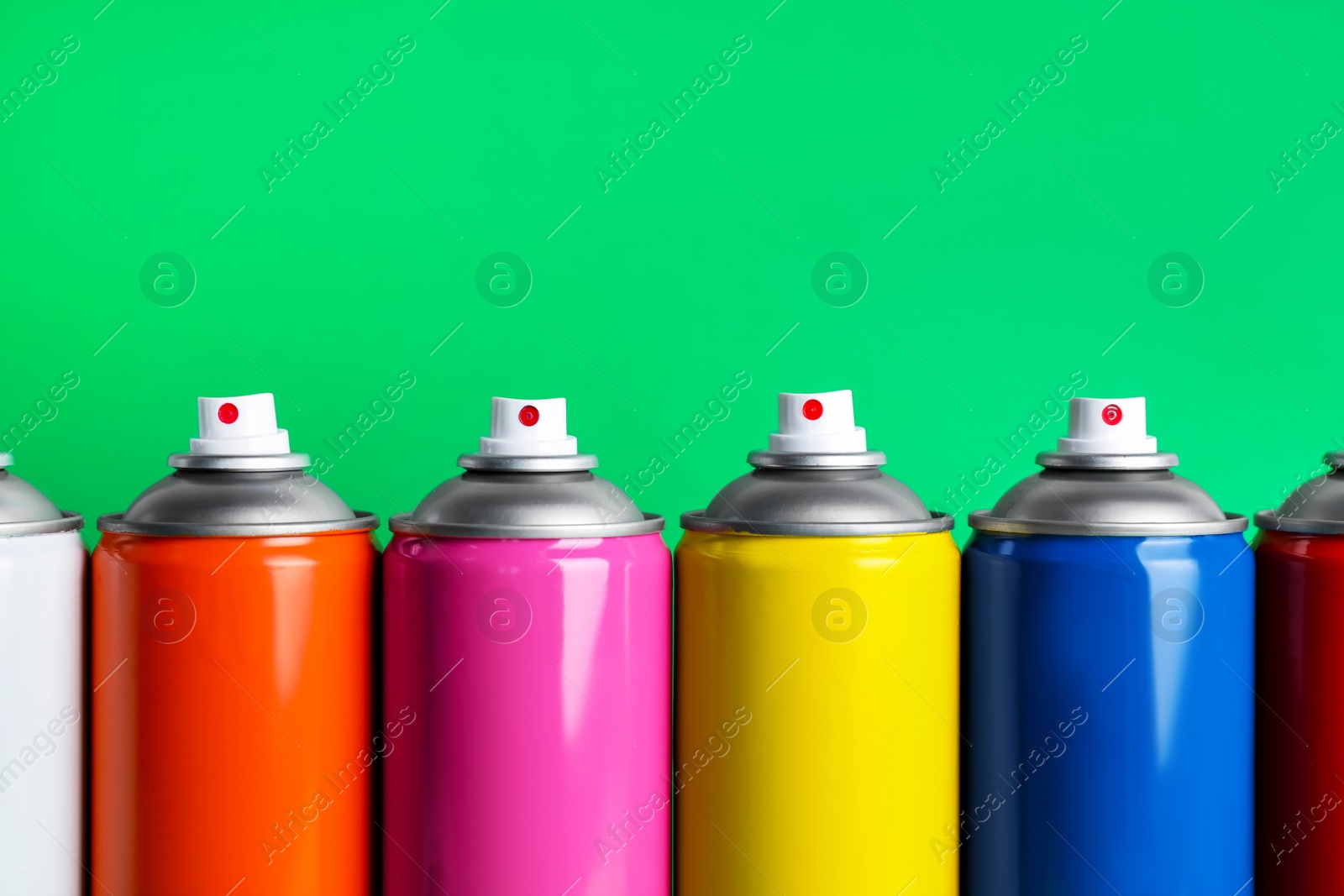 Photo of Colorful cans of spray paints on green background