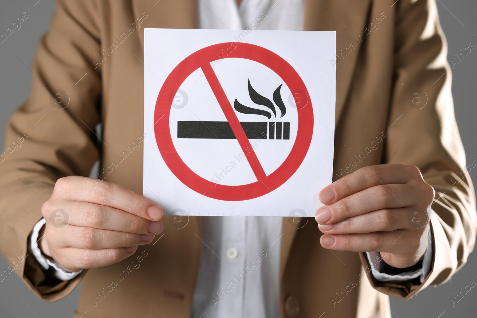 Photo of Woman holding card with no smoking sign on gray background, closeup